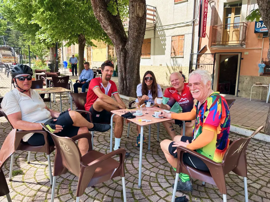 Cycling friends sharing coffee and laughs at an outdoor café under the trees in Abruzzo